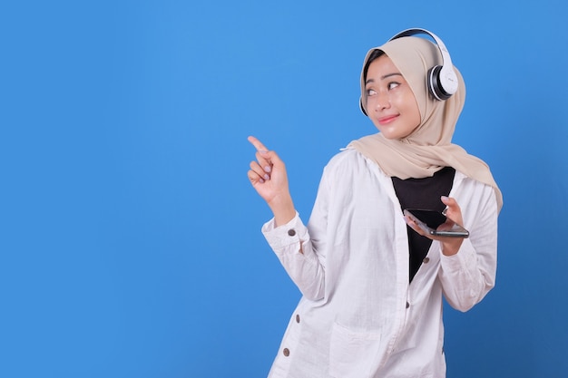 Happy beautiful girl dancing and listening music in wireless headphones, holding smartphone