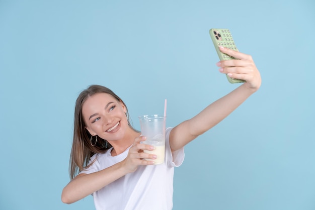 幸せな美しい女の子は携帯電話で新鮮なミルクセーキで自分の写真を撮ります