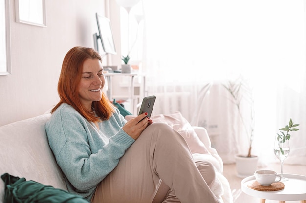 Happy beautiful girl using mobile phone, sitting in the living room.