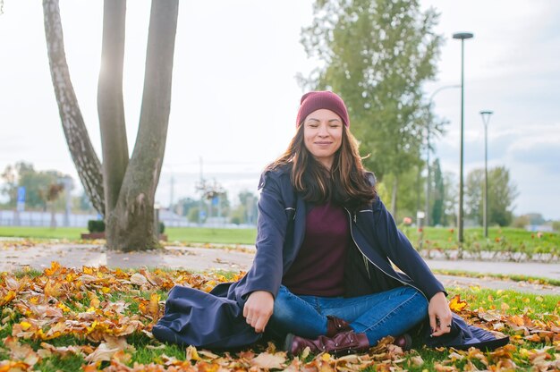 Happy Beautiful Girl zit in de herfst in gele bladeren op het gazon in de stad.