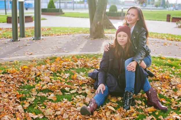 Happy Beautiful Girls zit in de herfst in gele bladeren op het gazon in de stad.