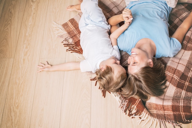 Happy and beautiful mother and child family together at home lie on a blanket on the floor