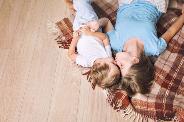 Happy and beautiful mother and child family together at home lie on a blanket on the floor