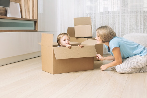 Happy and beautiful mother and child family together in a new home with cardboard boxes