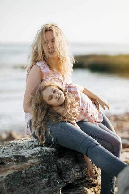 Foto felice bella madre e sua figlia che si divertono sulla spiaggia rocciosa al tramonto.