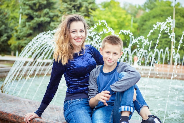 Photo happy beautiful mother and son enjoying near the fountain