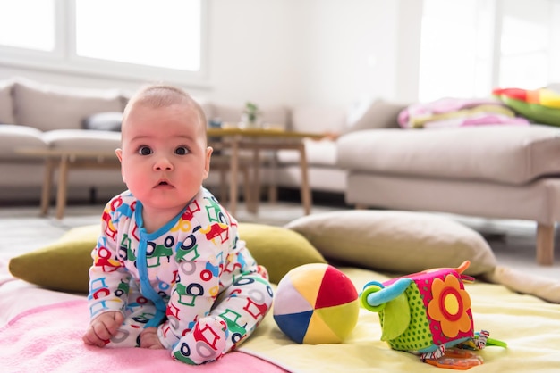 счастливый красивый новорожденный мальчик сидит на разноцветных одеялах, играя в первые игры на полу дома