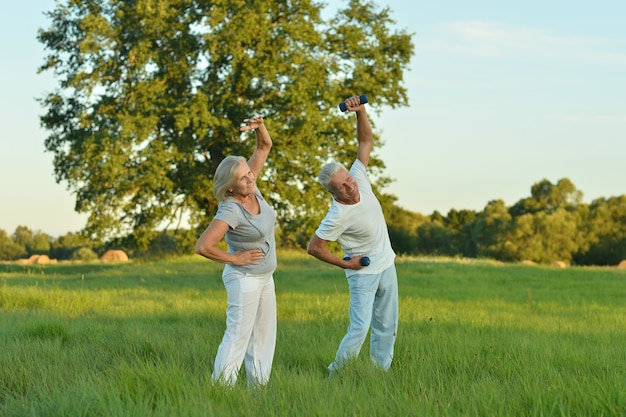 Happy beautiful senior couple exercising  in summer field