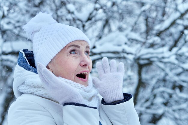 Foto felice bella donna anziana con un cappello caldo che posa in un parco invernale innevato