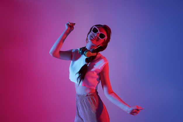 Happy beautiful teen woman listening music and dance on neon background