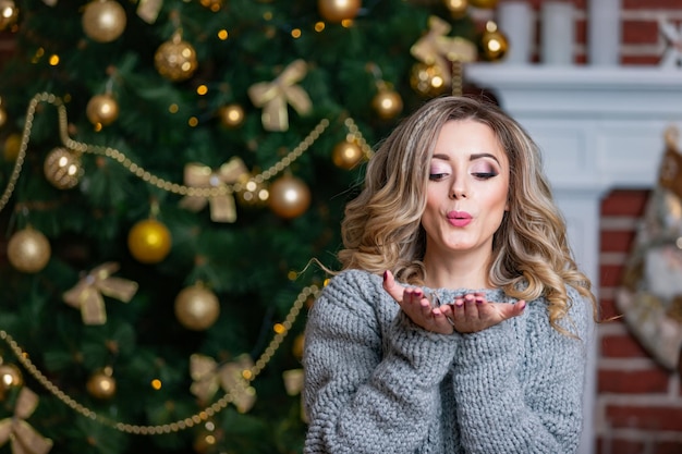 공이 있는 크리스마스 트리 배경에서 공기 키스를 보내는 회색 드레스를 입은 행복한 아름다운 여자 스톡 사진