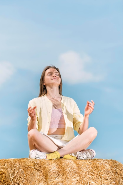 Happy beautiful woman sits in lotus position with closed eyes on haystack and meditates Countryside holiday