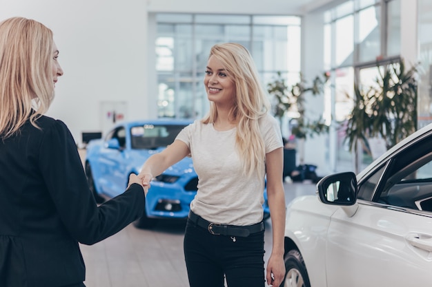 Bella donna felice che sorride stringe la mano al commerciante di automobile dopo l'acquisto della nuova automobile
