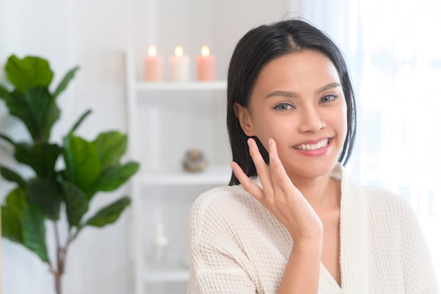 A happy beautiful woman in white bathrobe applying moisturizing cream on face