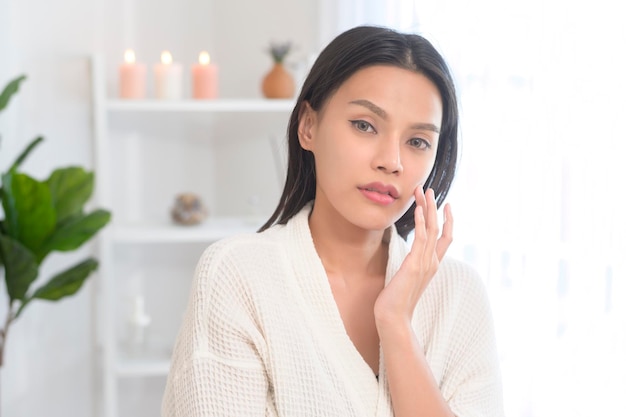 A happy beautiful woman in white bathrobe applying moisturizing cream on face