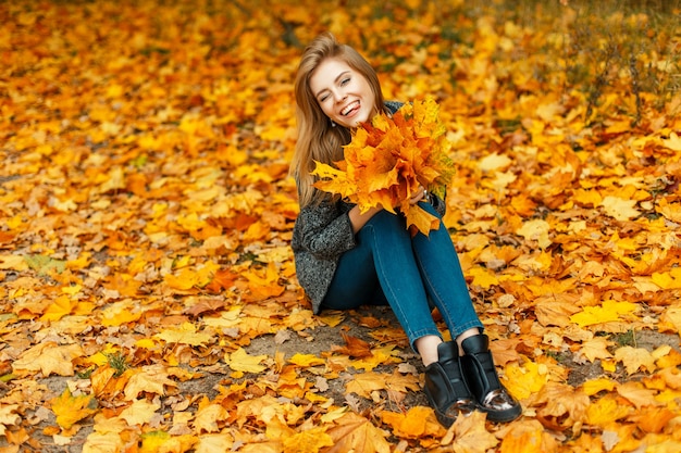 Happy beautiful woman with a bouquet of yellow foliage enjoying the moment in the autumn leaves