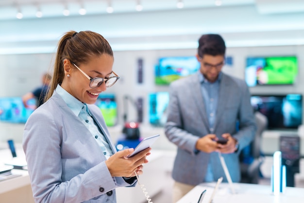 Bella donna felice con la coda di cavallo e vestita in vestito che compra nuovo smart phone