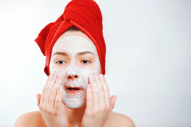 happy beautiful woman with a red towel on her head applies a scrub on the face of a large portrait on a white wall emotional gender role