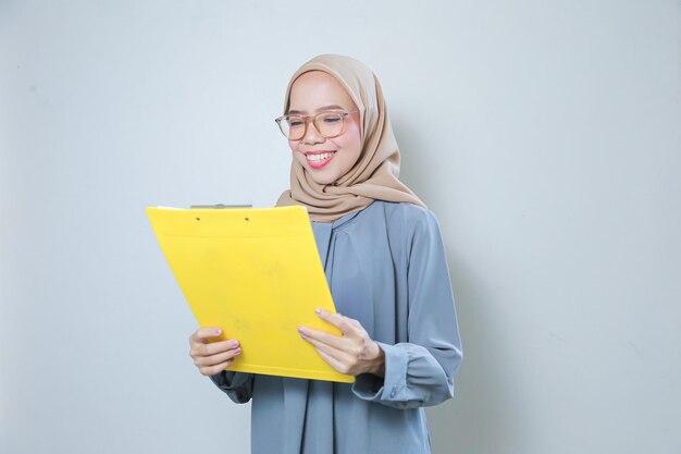 Happy beautiful young Asian muslim business woman wearing glasses holding clipboard