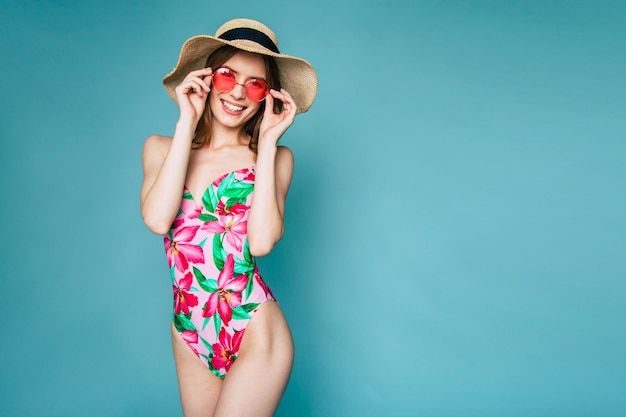 Happy Beautiful young blonde woman standing on blue background in swimsuit or bikini and smiling while posing. Summertime and vacation