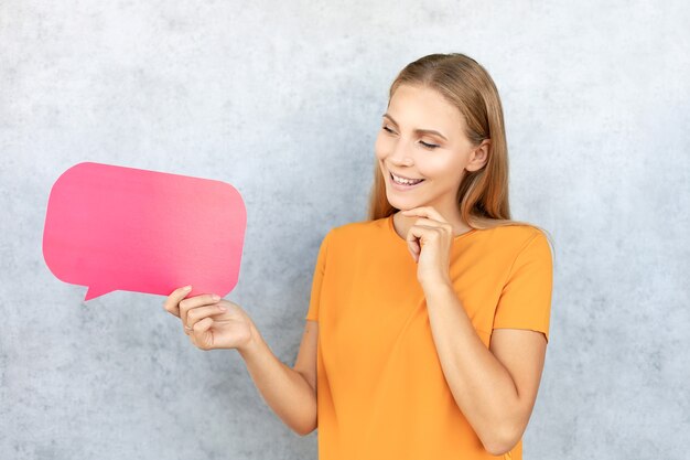 Photo happy beautiful young blonde woman standing isolated over gray background, holding empty speech bubble.