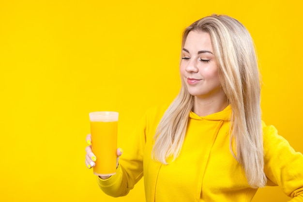 Happy beautiful young blonde woman in yellow casual sporty clothes holding orange juice glass,