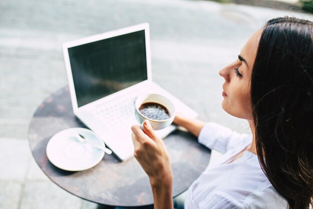 Foto felice bella giovane donna di affari che lavora al computer portatile in street cafe all'aperto