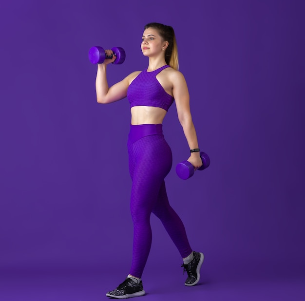 Happy. Beautiful young female athlete practicing , monochrome purple portrait. Sportive fit caucasian model with weights. Body building, healthy lifestyle, beauty and action concept.