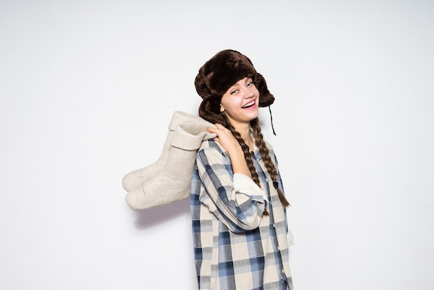 Happy beautiful young russian girl in fur hat holds gray felt boots in hands, laughs