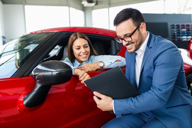 車のショールームで新しい車を買う幸せな美しい若い女性。