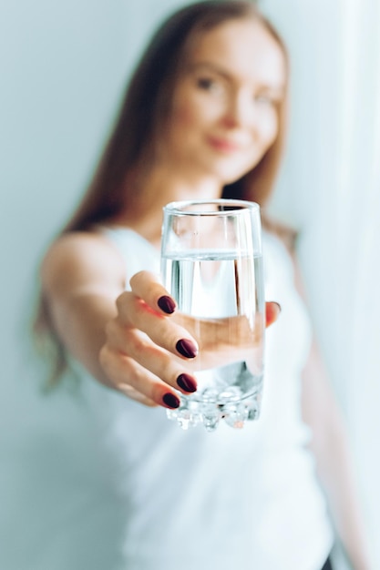 Happy beautiful young woman drinking water Smiling caucasian female model holding transparent glass in her hand Closeup Focus on the arm