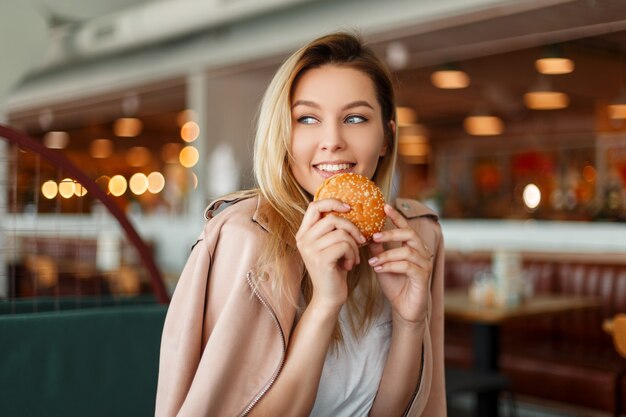 屋内でハンバーガーを食べる幸せな美しい若い女性