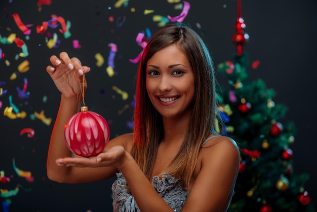 Happy beautiful young woman holding red Christmas baubles. Selective focus. Looking at camera.