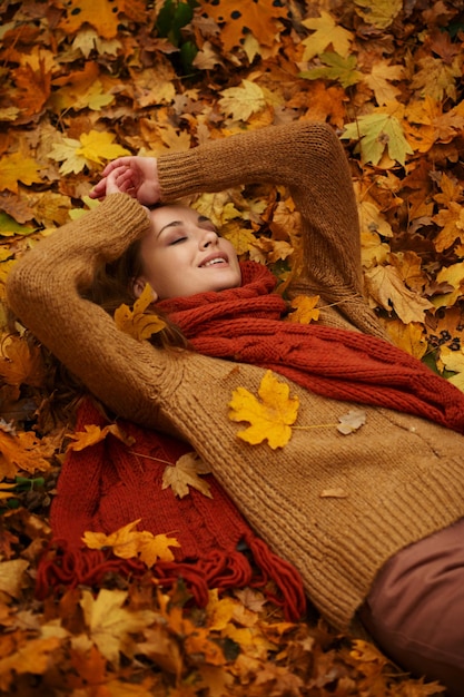 Happy beautiful young woman lying on gold autumn maple leaves enjoy warm weather. Outdoor portrait