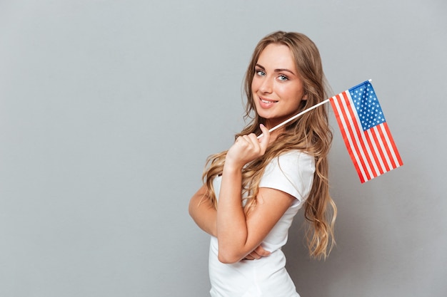 アメリカ合衆国の旗を立てて保持している幸せな美しい若い女性