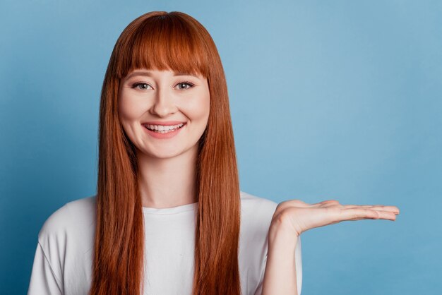 Happy beautiful young woman wear t-shirt holding on palm isolated on blue background with copy space