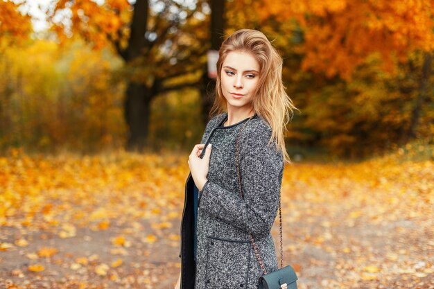 Happy beautiful young woman with a smile in a trendy coat posing in a yellow autumn park