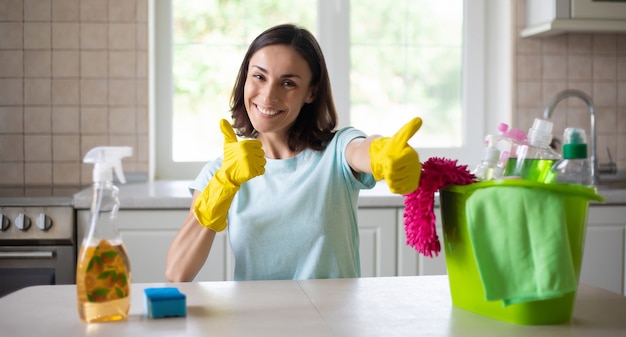 Felice bella giovane donna in guanti gialli sta pulendo la cucina con attrezzature speciali e spray