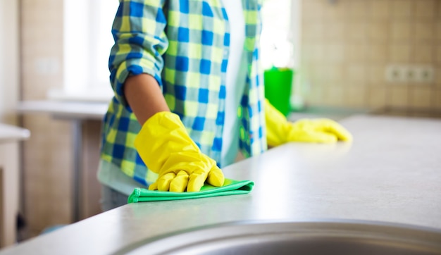 黄色い手袋をはめて幸せな美しい若い女性は、特別な機器とスプレーでキッチンを掃除しています