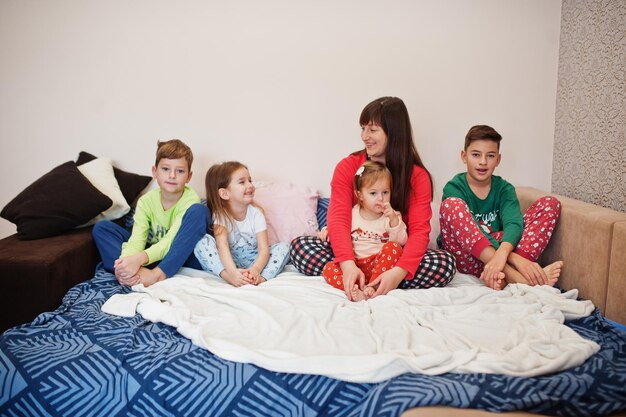 Happy big family is having fun together in bedroom. Large family morning concept. Mother with four kids wear pajamas in bed at home.