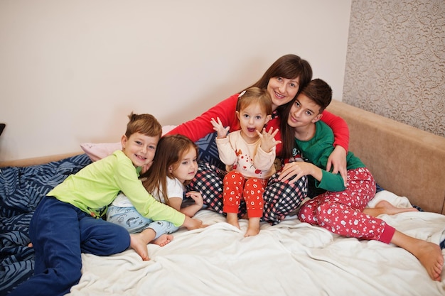 Happy big family is having fun together in bedroom. Large family morning concept. Mother with four kids wear pajamas in bed at home.