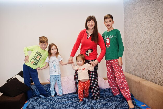 Happy big family is having fun together in bedroom. Large family morning concept. Mother with four kids wear pajamas in bed at home.