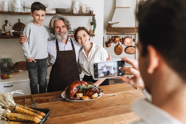 Счастливая большая семья позирует для фотоаппарата, стоя за кухонным столом и празднуя Сочельник