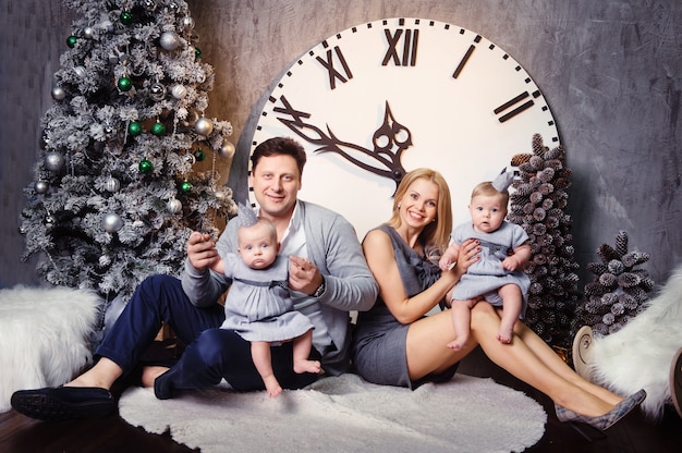 A happy big family with twin children in the New Year's interior of the house against the background of a large clock