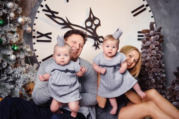 A happy big family with twin children in the New Year's interior of the house against the background of a large clock