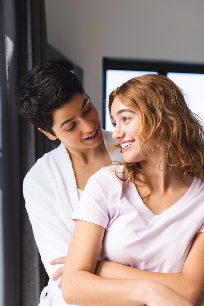 Foto una felice coppia lesbica biraciale che si abbraccia al sole vicino alla finestra di casa.