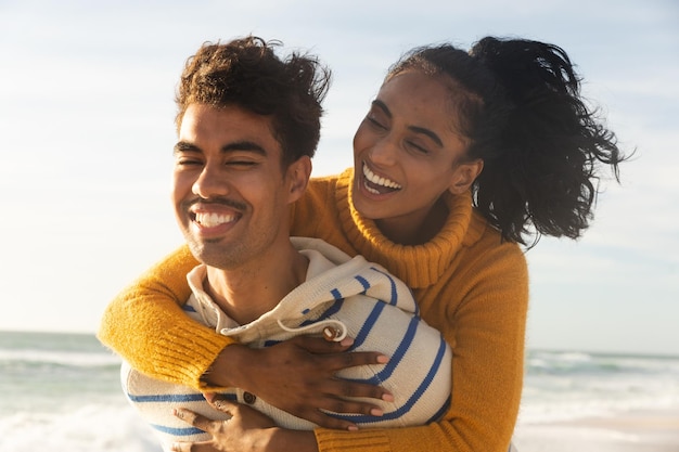 Happy biracial man giving piggyback ride to girlfriend at beach on sunny day