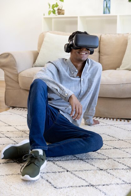 Happy biracial man using vr headset sitting on floor at home