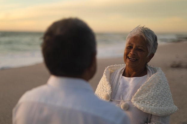 Happy biracial senior woman looking man during wedding ceremony at beach