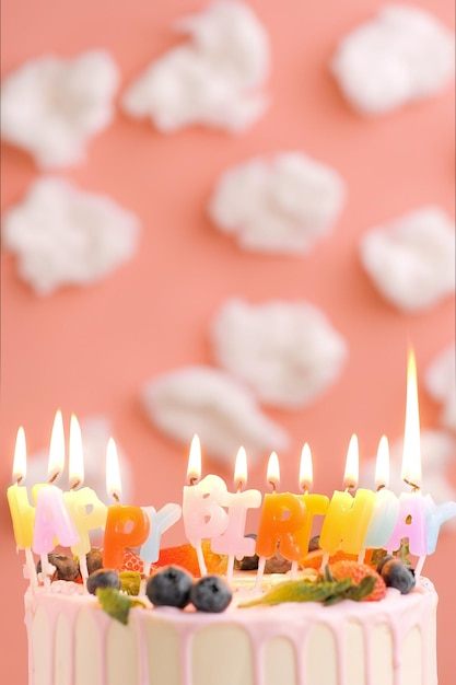 Happy birthday cake beautiful cake with candle title happy\
birthday on pink background with white clouds closeup and vertical\
view